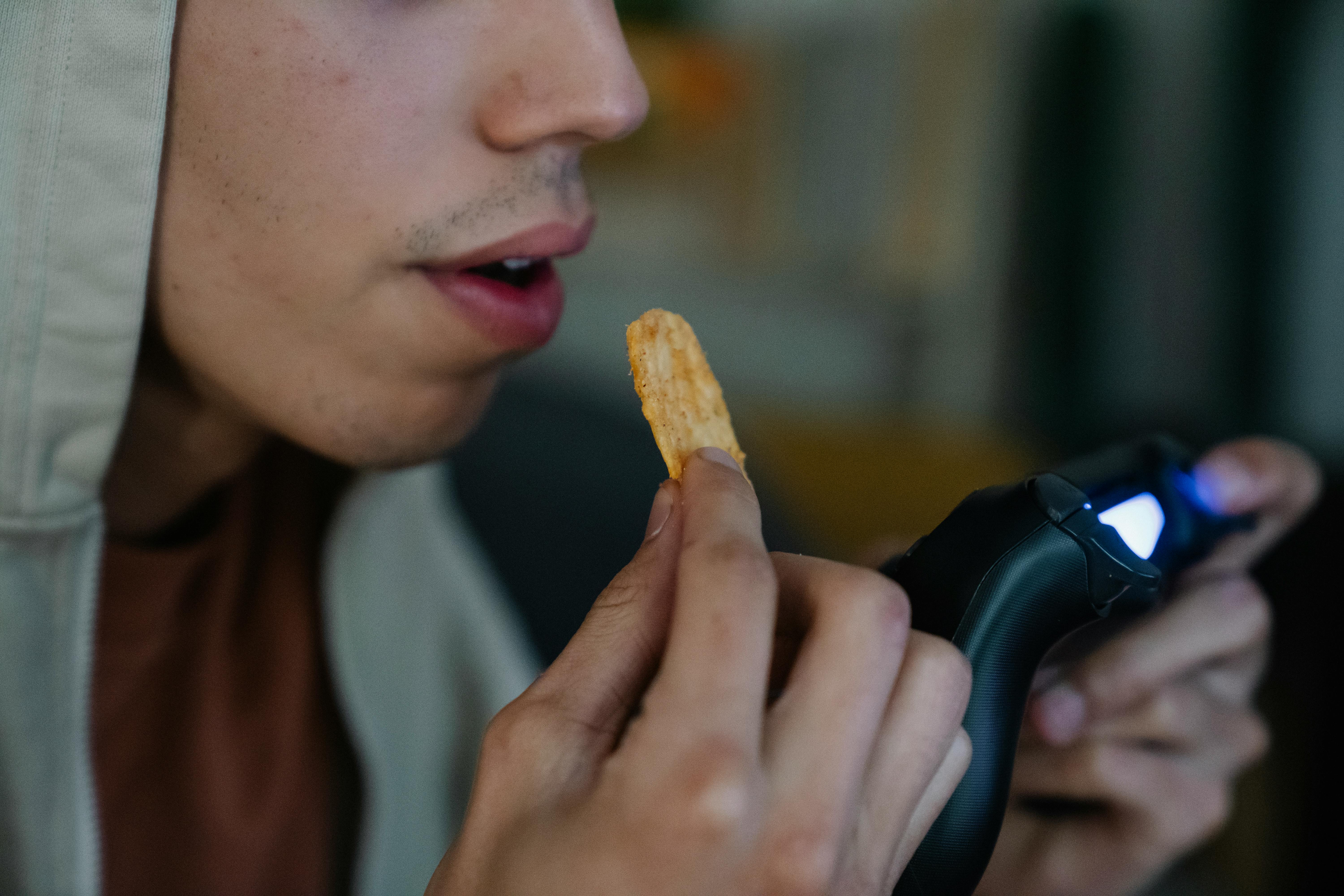 Young man playing videogames and eating chips | Source: Pexels